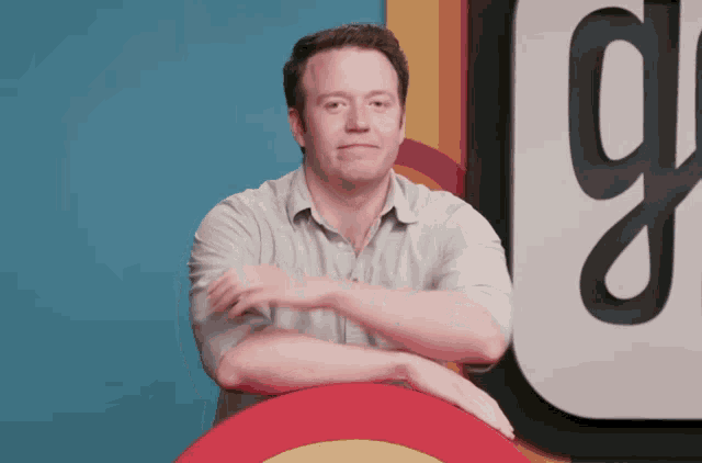 a man with his arms crossed stands in front of a sign that has the letter g on it