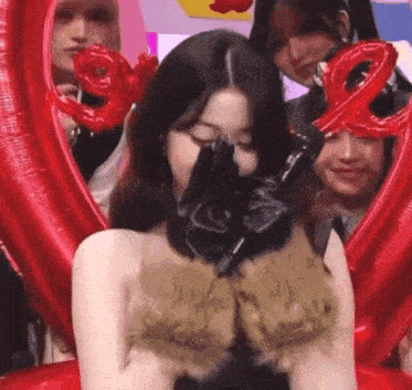 a woman wearing a black glove is standing in front of a group of people holding red balloons .