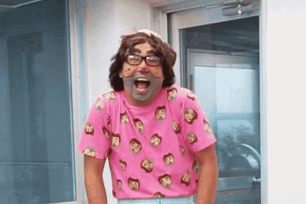 a man wearing glasses and a pink shirt with faces on it is standing in front of a door .