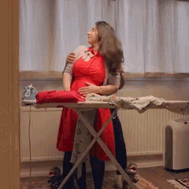 a woman in a red dress is standing in front of an ironing board with clothes on it