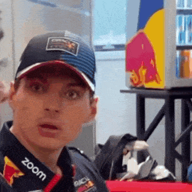 a man wearing a hat and a red bull shirt is looking at the camera .