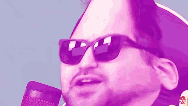a man wearing sunglasses and a hat is talking into a pink microphone