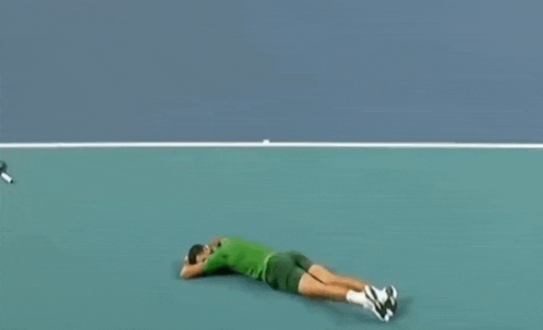 a man is laying on the ground on a tennis court while holding a tennis racket .
