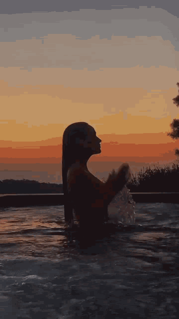 a woman is standing in a pool with a sunset in the background