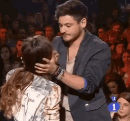 a man is touching a woman 's face in front of a crowd with the number 1 in the corner