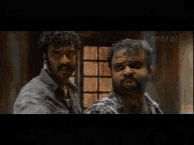two men are standing next to each other in a room and looking at each other .