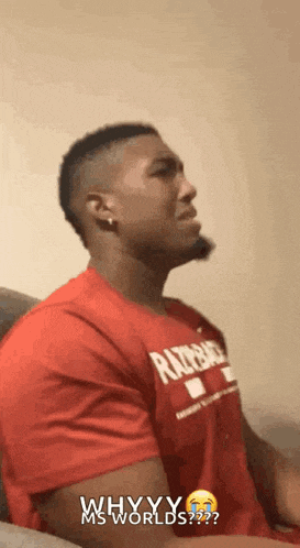a man in a red shirt is sitting on a couch and says " why yy ms worlds "
