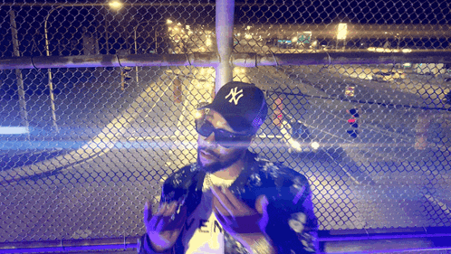 a man wearing a ny hat stands in front of a fence
