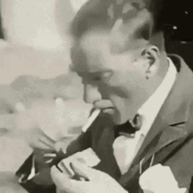 a man in a suit is smoking a cigarette while looking at his phone