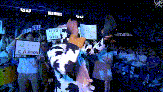 a man in a cow suit holds up a sign that says keyz to win
