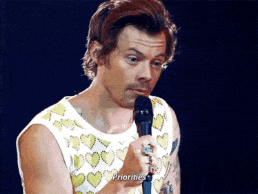 a man in a tank top is holding a microphone and saying " priorities " .