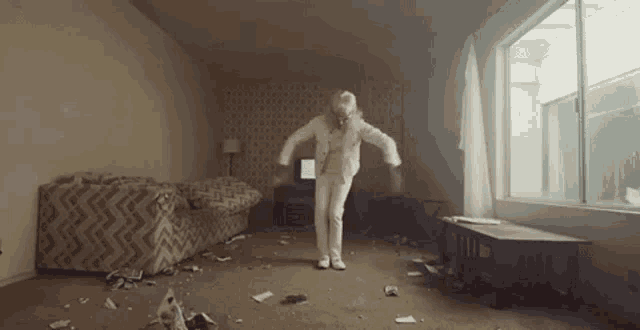 a man is dancing in a living room with a couch and a window .