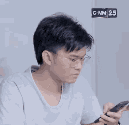 a young man wearing glasses is holding a cell phone in his hand while another person brushes his hair .