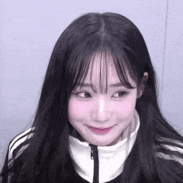 a girl with long black hair and bangs is wearing a black and white jacket and smiling .