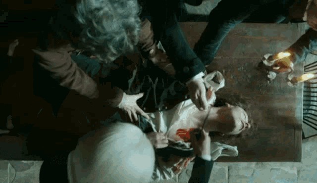 a group of people are gathered around a woman laying on the floor with blood on her chest