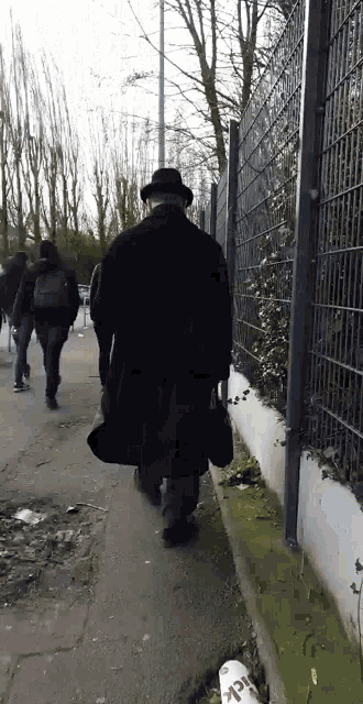 a man in a black coat and hat walks down a street