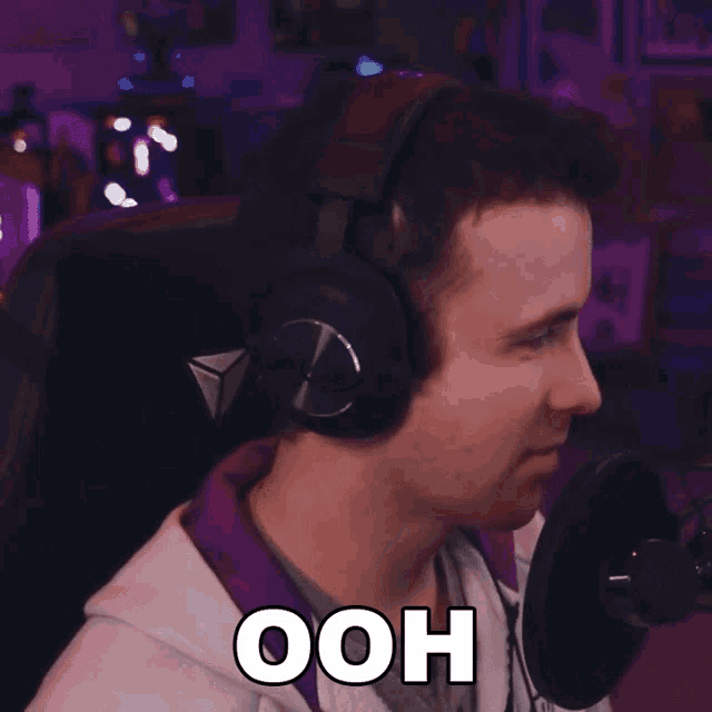 a man wearing headphones and a hoodie says ooh in front of a microphone