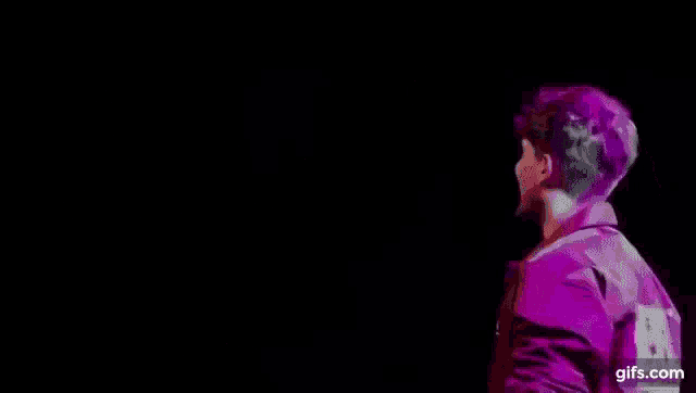 a man in a pink jacket is standing in front of a stage with purple lights .
