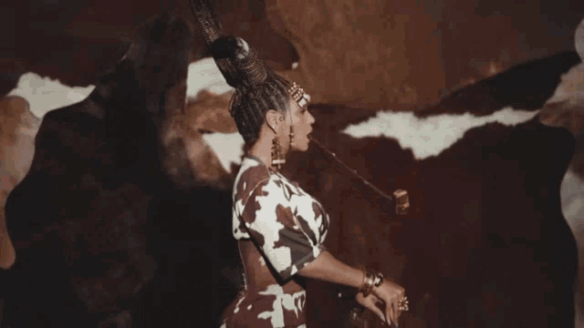 a woman wearing a cow print shirt and earrings is standing in front of a rock