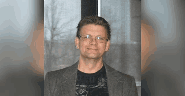 a man wearing glasses and a black shirt is smiling