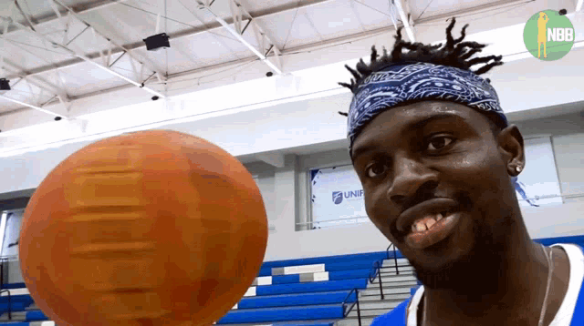 a man wearing a bandana looks at a basketball in front of a sign that says nba