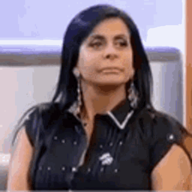 a woman in a black shirt and earrings is sitting on a couch .