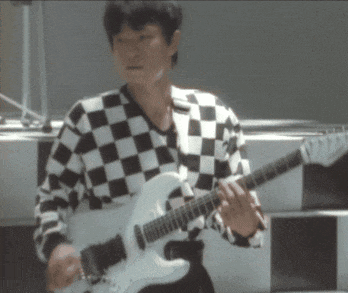a man wearing a black and white checkered shirt is playing a guitar