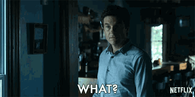 a man in a blue shirt is standing in front of a door and says what