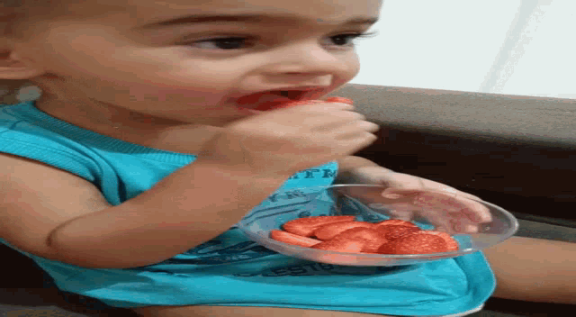 a little boy is eating strawberries from a bowl