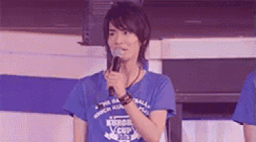 a man in a blue shirt is holding a microphone and speaking into it .