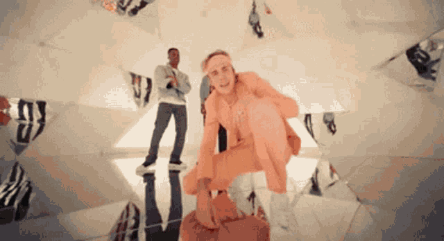 a man is kneeling down in front of a mirror with a man standing in the background