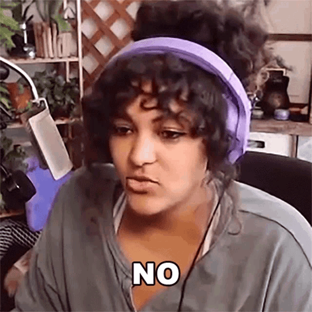 a woman wearing purple headphones is sitting in front of a microphone and says no .