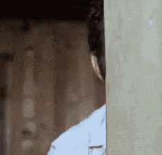 a man is peeking out of a doorway and looking at the camera .