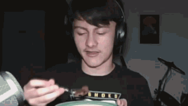 a young man wearing headphones is eating food from a plate with a fork .