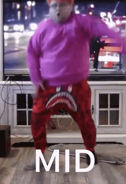 a man in a pink sweater and red pants is dancing in front of a television with the word mid written on the floor