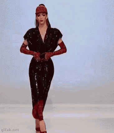 a model is walking down the runway at a fashion show wearing a red dress .