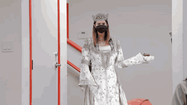 a woman wearing a white dress and a crown is wearing a mask
