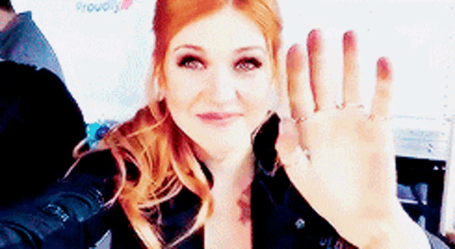a woman with red hair is waving her hand in front of a sign that says proudly on it