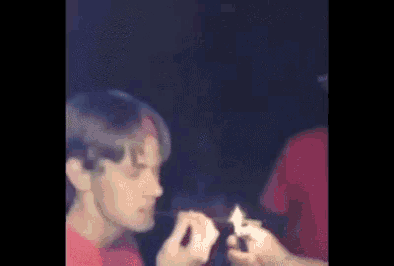 a man is smoking a cigarette in a dark room while another man holds a lighter .