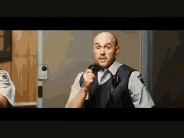a bald man in a police uniform is holding a microphone and talking into it .