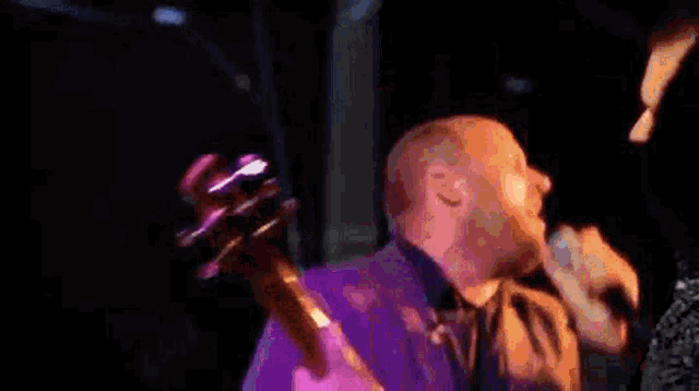 a man with a beard is singing into a microphone while another man looks on .