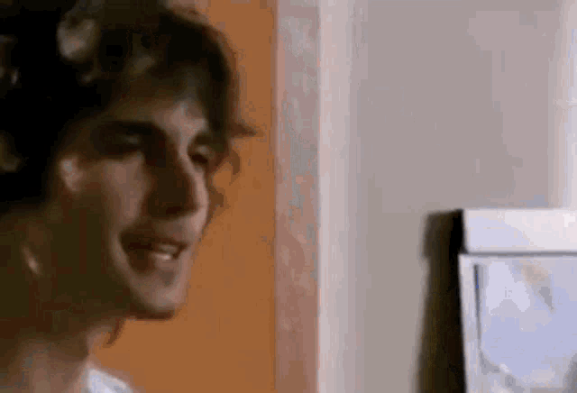 a man with curly hair is standing in front of a wall with a picture on it .