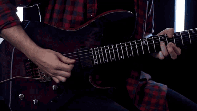 a man in a plaid shirt is playing a purple electric guitar with the letter k on the neck
