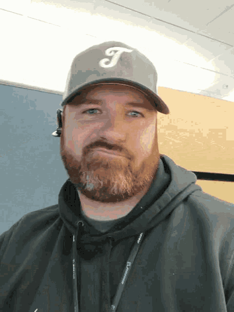a man with a beard is wearing a hat with the letter t on it