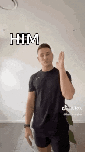 a man in a black shirt and shorts is standing in front of a white wall and giving a high five .