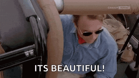 a man wearing sunglasses is sitting in a car with the words `` it 's beautiful '' written on the screen .