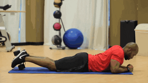 a man in a red shirt is doing a plank on a mat