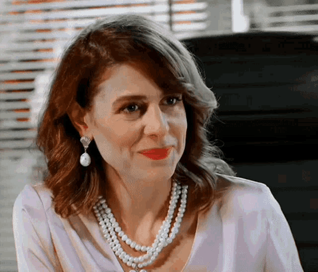 a woman wearing a pearl necklace and earrings looks at the camera