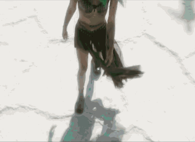 a woman in a bikini is walking through the snow holding a fan .