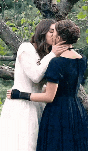 two women are kissing in front of a tree .